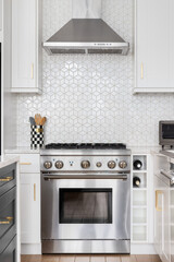 Fototapeta premium A kitchen stove detail shot in a luxury kitchen with white cabinets, stainless steel appliances, and pattern tile backsplash.