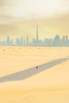 View from above, stunning aerial view of a person walking on a deserted road covered by sand dunes with the Dubai Skyline in the distance. Dubai, United Arab Emirates.