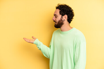 young adult bearded man feeling happy and smiling casually, looking to an object or concept held on...
