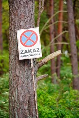 Selective focus shot of a road "Zakaz Parkowania" or no parking sign in the forest