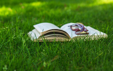 Open book with eyeglasses on the green grass. Natural healthy lifestyle with good eyesight.