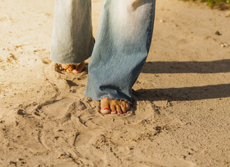 Sunny beach, bare female feet with pink nails walk on the sand.