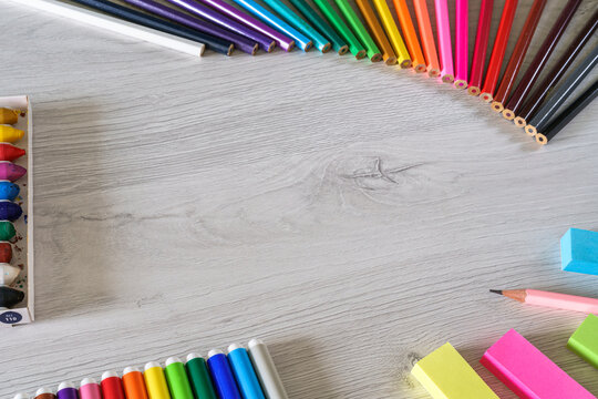 Close-up of colorful pencils making a rainbow and supplies for back to school kids on a wooden table