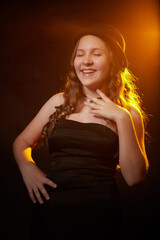 Fototapeta premium Portrait of an elegant nice fun happy teenager girl in a black hat and dress. Studio shot. Posing woman in a hat and black dress. A long haired girl shows a slender figure