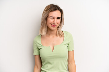 young adult blonde woman looking happy and friendly, smiling and winking an eye at you with a...