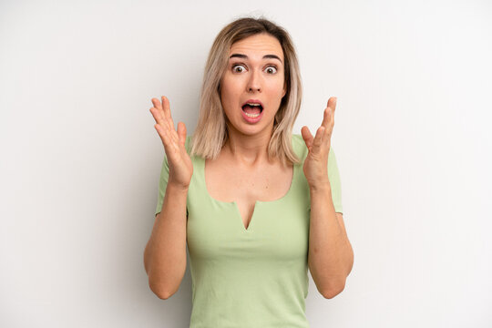 young adult blonde woman looking shocked and astonished, with jaw dropped in surprise when realizing something unbelievable