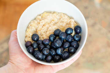Cook at home. Plate with oatmeal and blueberries in hand.