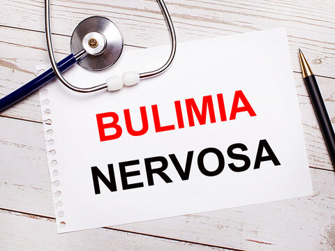 On a light wooden table there is a stethoscope, a pen and a sheet of paper with the text BULIMIA NERVOSA. Medical concept