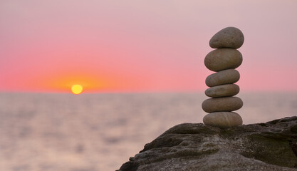 Stacked stone tower on the beach by the sea with the sunset out of focus.