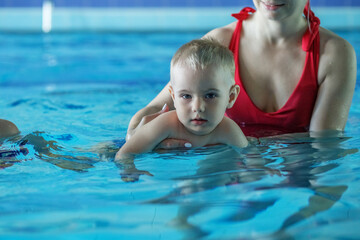 Small child boy is studying in swimming pool with support of mom.