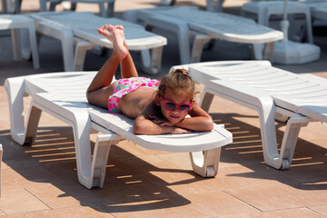 Little cute girl in sunglasses, near the pool.