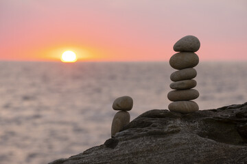 Stacked stone tower on the beach by the sea with the sunset out of focus.