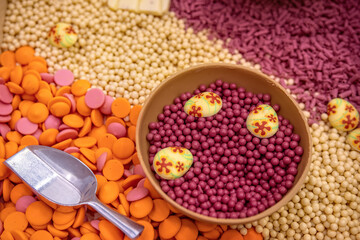 Ruby chocolate dragee in bowl of chocolate on background of colored chocolate drops.