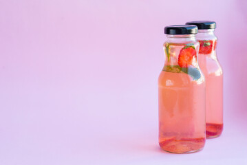Fototapeta na wymiar Homemade strawberry mint lemonade in two glass bottles to go. Eco packaging, reusable dishes zero waste concept. Natural healthy alcohol free drink recipe for hot summer on pink background