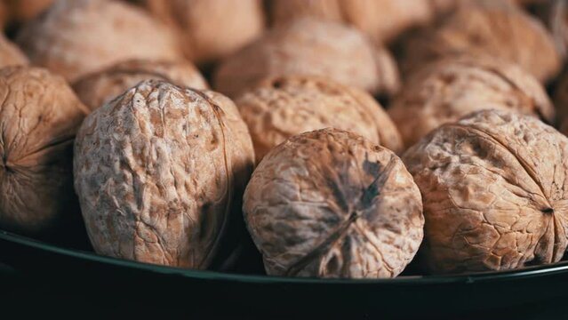 Lot of walnuts in the shell are spinning on a black background. Nuts are good for the brain. Heap of walnuts close-up.