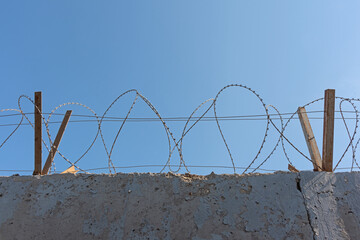 Barbed wire on a cement wall of a fence against a blue sky