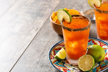 Homemade michelada cocktail with beer, lime juice,hot sauce,salted rim and tomato juice on wooden table. Copy space
