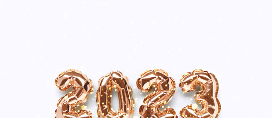 Banner with shiny 2023 gold inflatable balloons on a blue background with copy space. New Year's festive concept.