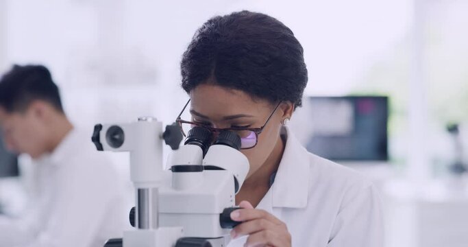 Female scientist using a microscope with glasses in a research lab. Young biologist or biotechnology researcher working and analyzing microscopic samples with the latest laboratory tech equipment