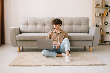 Portrait of attractive young curly hair man using laptop while sitting on sofa at home