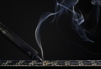 Backdrop of smoking soldering iron on dark background.