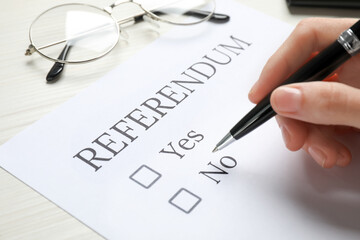 Woman with referendum ballot making decision at white table, closeup