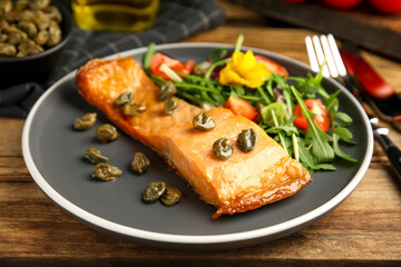 Tasty cooked salmon with capers and salad served on wooden table, closeup