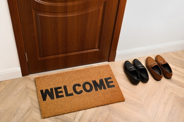 New clean brown mat with word Welcome and shoes near entrance door