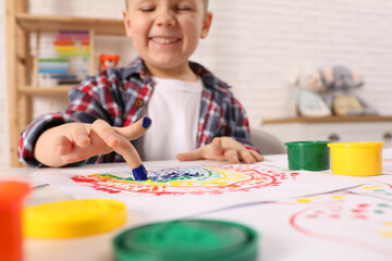 Little boy painting with finger at white table indoors, focus on hand