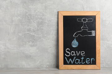 Blackboard with words Save Water and drawn tap on grey table. Space for text
