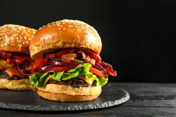 Tasty burgers on black wooden table, closeup with space for text. Fast food