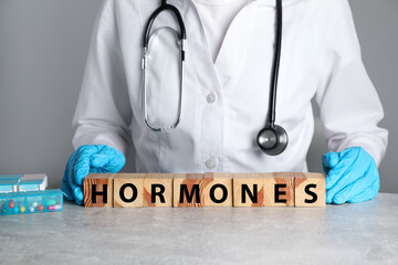 Doctor near word HORMONES made with wooden cubes at grey table, closeup