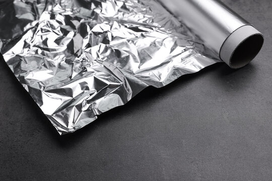 Roll of aluminum foil on dark grey table, closeup