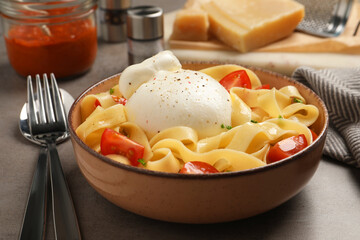 Bowl of delicious pasta with burrata and tomatoes on grey table