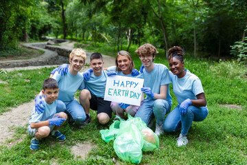 Diverse Group of People Picking Up Trash in The Park Volunteer Community Service. Happy international volunteers holding placard with 'happy Earth day' message.