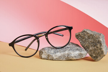 eye glasses on a concrete podium on a pink and beige background, trend composition, black stylish eye glasses,