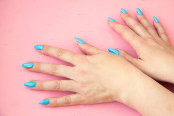 Two hands with a blue manicure on a pink background flat lei