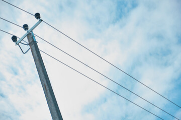 High voltage electric pylon and electrical wire at green rice field and tree forest with overcast sky