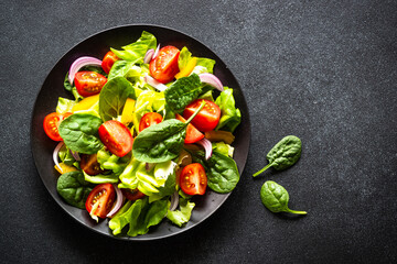 Green salad with fresh vegetables and green leaves at black background. Top view with copy space.