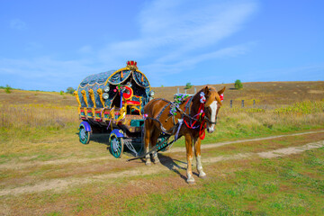 a horse with a brightly decorated wagon in a field - obrazy, fototapety, plakaty