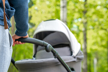 A man is driving a baby carriage. A young father walks with a newborn baby in a stroller on a summer day