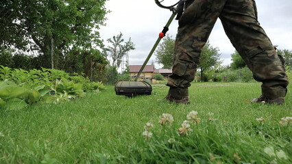 A gardener mows the grass in the garden with a brushcutter.
Ogrodnik kosi trawę w ogrodzie za pomocą wykaszarki. - obrazy, fototapety, plakaty