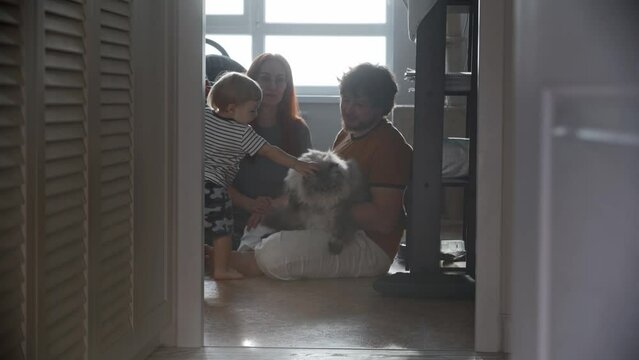Happy family sitting on the floor and their fluffy cat comes to them
