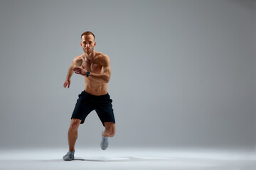 Developing endurance. Male athlete in motion isolated over gray studio background. Maintaining health and strength. Concept of sport, healthy lifestyle, motion