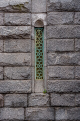 Narrow window with a green iron grate in a niche of an old gray stone wall. From the Window of the World series.