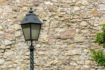 Street electric lamp on the background of an old stone wall. The background is a bit blurry.
