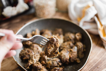 homemade fried liver on a fork held in your hand in the kitchen (selective focus, blurred background)