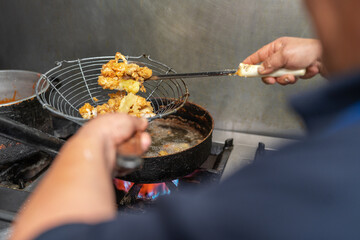 Cook picking chunks of meat and fish from a pan using a strainer