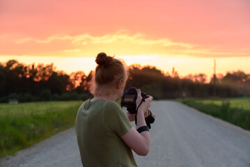 a young male photographer takes pictures on a dirt road in a red sunset on a summer evening
