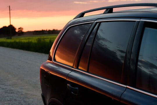 SUV on off-road rocky road. A beautiful red summer evening sunset is reflected in the SUV's tinted rear windows. Close-up.